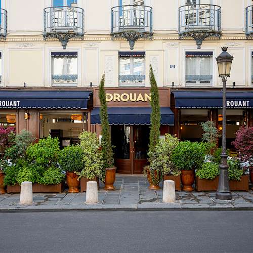 Restaurant charmant Drouant avec une façade classique parisienne, grandes fenêtres, et plantes en pot, offrant une atmosphère accueillante.