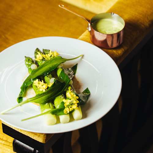 Plat frais à base de légumes tendres légèrement cuits, agrémenté d'herbes finement hachées et d'une vinaigrette crémeuse servie à part, offrant un équilibre de textures et de saveurs.