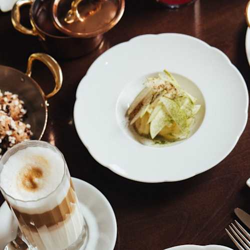 Plat délicat de laitue finement hachée, légèrement assaisonnée et garnie de noix, accompagné d'une sauce crémeuse. Présenté avec un verre de café en couches et un petit bol de fruits.