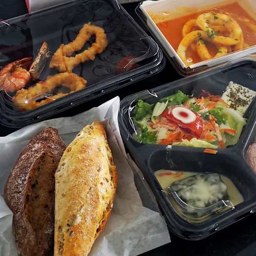 Assortiment van gerechten in afhaalverpakkingen, waaronder krokante garnalen en calamares, calamares in een rijke oranje saus, een gevulde bladerdeegpastei en een frisse salade met gemengde groenten, cherrytomaten en radijs, geserveerd met een romige dressing en yoghurtdip.