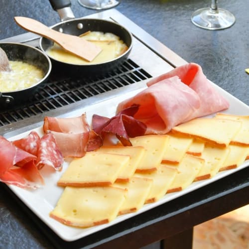 Plateau joliment présenté avec un assortiment de viandes séchées, incluant du prosciutto et du salami, accompagné de fromages semi-mous et de pommes de terre rôties dorées.