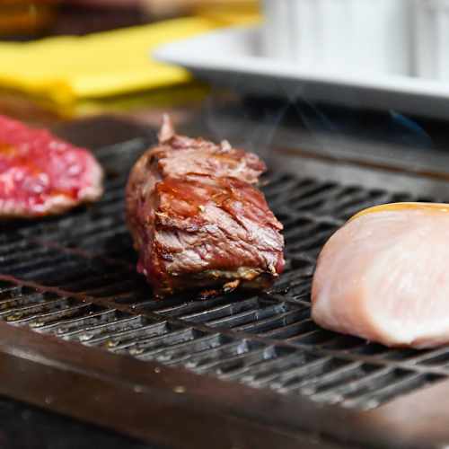 Grill avec trois morceaux de viande : un morceau de bœuf cru, un bœuf cuit légèrement grillé, et un blanc de poulet grillé à la perfection.