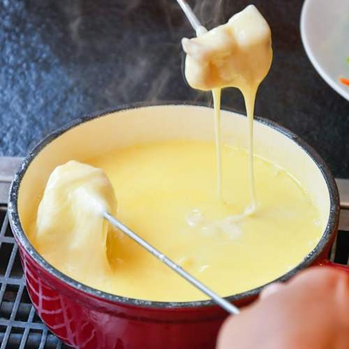 Pot de fromage fondu crémeux, probablement un mélange de Gruyère et d'Emmental, accompagné de pain et d'une salade fraîche.