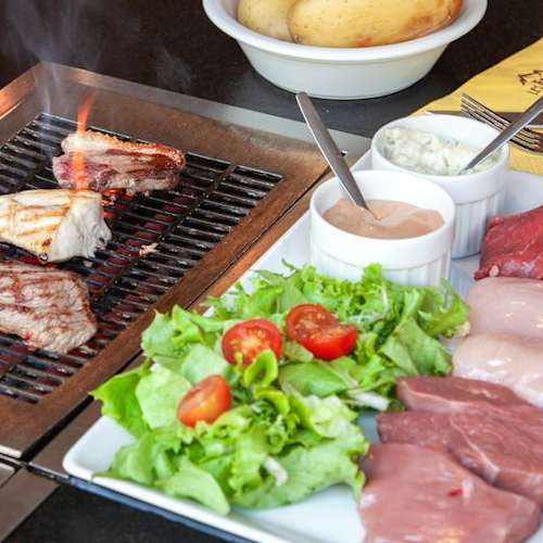 Sélection de viandes crues et d'ingrédients frais pour le grill, comprenant des morceaux de bœuf, de poulet et possiblement de porc, accompagnés d'une salade croquante et de sauces.