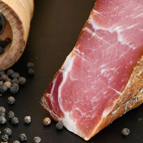 Jambon bien affiné, de couleur rose profond avec du gras marbré, accompagné de grains de poivre noir, suggérant une expérience savoureuse et aromatique.