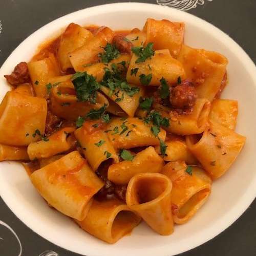 Plat copieux de pâtes en forme de tubes larges, enrobées d'une sauce tomate épaisse, agrémentées de morceaux de viande et de fines herbes fraîches.