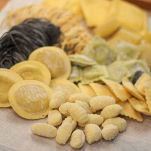 Assortiment de pâtes fraîches comprenant des raviolis jaunes crémeux, des gnocchis dodus, des pâtes colorées au goût d'épinard et d'encre de seiche, ainsi que des feuilles plates pour lasagne et des tortellinis, mettant en avant la qualité artisanale et la diversité.