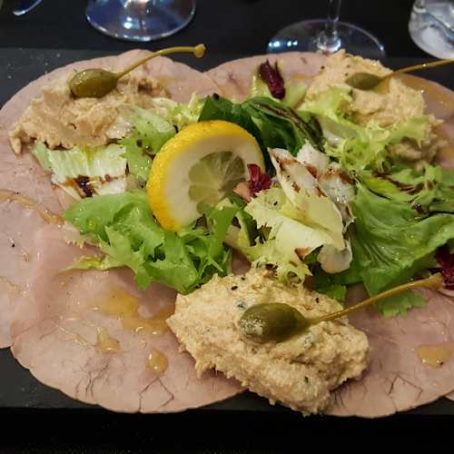 Plat de bœuf tendre tranché finement, accompagné d'une sauce crémeuse à la moutarde, de câpres, de légumes frais et d'une tranche de citron, offrant une présentation élégante et équilibrée.