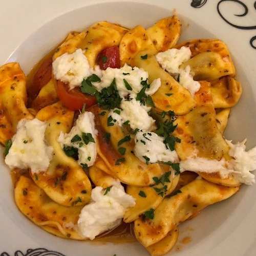 Assiette de pâtes avec de grands raviolis farcis, nappés d'une sauce tomate épaisse, garnis de ricotta crémeuse et de persil frais haché.