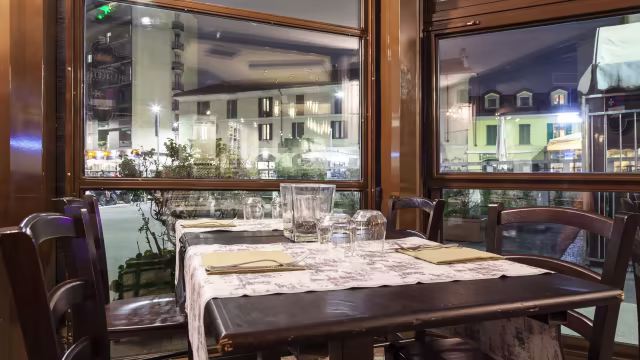 Interno di un ristorante accogliente con tavolo di legno, tovaglia elegante e posate ordinate, che offre un'atmosfera calda e invitante.