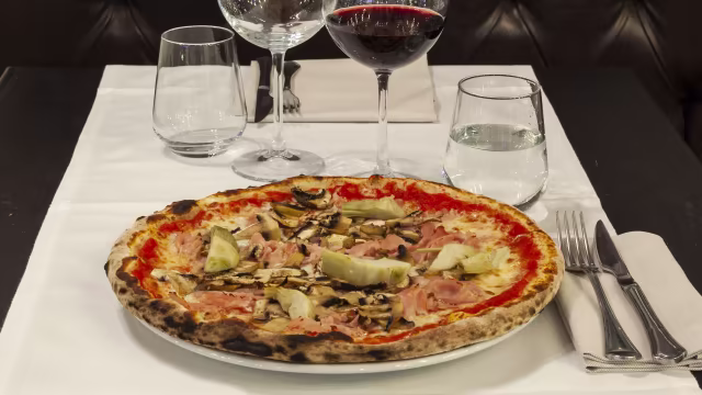 Pizza classica con crosta dorata, salsa di pomodoro, fette di prosciutto, funghi e cuori di carciofo, con formaggio fuso e leggermente frizzante.