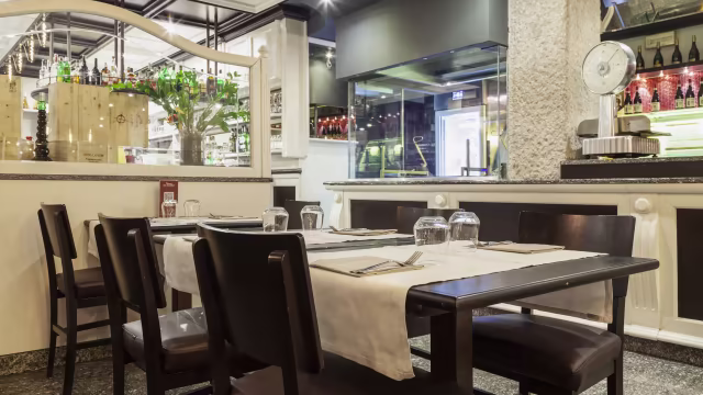 Interno di un ristorante moderno con tavoli ben disposti, sedie in legno scuro e un bar ben fornito, che crea un'atmosfera accogliente e sofisticata.