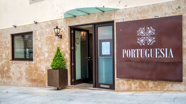 Exterior do restaurante "Portuguesia" com uma porta de madeira, fachada de pedra clara, arbusto verde e lanterna decorativa.