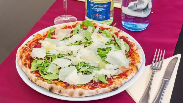 Pizza recién horneada con salsa de tomate, rúcula fresca y queso parmesano rallado sobre una base crujiente.