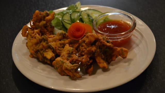 Gouden groentefritters geserveerd met een zoete en pittige dipsaus, vergezeld van een frisse salade met komkommer, bladgroenten en een decoratieve wortelkrul.