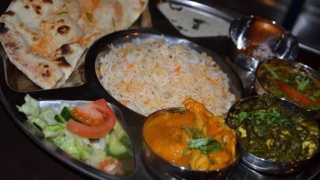 Traditionele Indiase maaltijd met geurige basmatirijst, omringd door drie curry's: boterkip in romige saus, palak paneer met spinazie en paneer, en gemengde groentecurry. Geserveerd met een frisse salade en naanbrood.