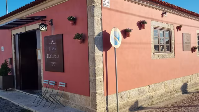 Exterior de um restaurante encantador com uma fachada em tom pêssego, detalhes em pedra e vasos de flores nas paredes, criando um ambiente acolhedor e convidativo.