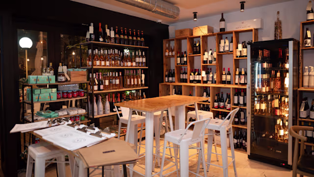 Tienda de vinos acogedora con estanterías de madera llenas de botellas, iluminación cálida y una mesa central para degustaciones.