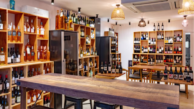 Tienda de vinos moderna con estanterías de madera, botellas de vino variadas y una atmósfera cálida gracias a la iluminación.
