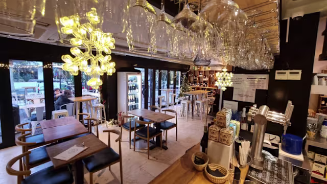 Interior moderno de restaurante con barra de madera, iluminación cálida y mesas de madera con sillas negras.