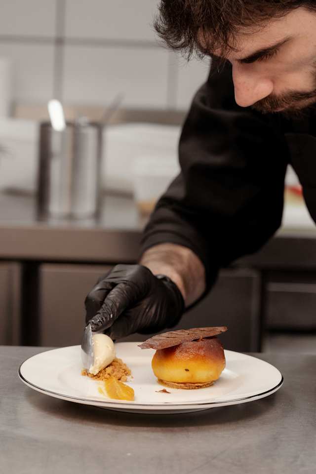 Dessert composé d'une pâtisserie dorée et ronde, garnie d'une crème, accompagnée d'une boule de glace à la vanille et d'un filet de sauce aux fruits.