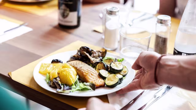 Salmone perfettamente cotto con crosta dorata, accompagnato da zucchine saltate e fette di arancia, guarnito con erbe fresche.