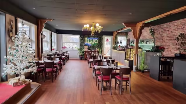 Das Restaurant bietet eine warme und einladende Atmosphäre mit Holzböden und einer Mischung aus rustikalem und modernem Dekor. Die Tische sind ordentlich angeordnet und schaffen ein gemütliches Speiseerlebnis. Ein großes Fenster lässt natürliches Licht herein, während eine dekorative Weihnachtsbaum-Ecke festliche Akzente setzt. Exponierte Ziegelwände und Pflanzen tragen zu einem entspannten, stilvollen Ambiente bei.