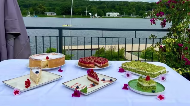 Auswahl an kunstvoll präsentierten Desserts: klassischer Käsekuchen, Himbeerkuchen mit roter Beerenfüllung und Pistazienkuchen mit knackigem Nuss-Topping, garniert mit essbaren Blumen und frischen Beeren.