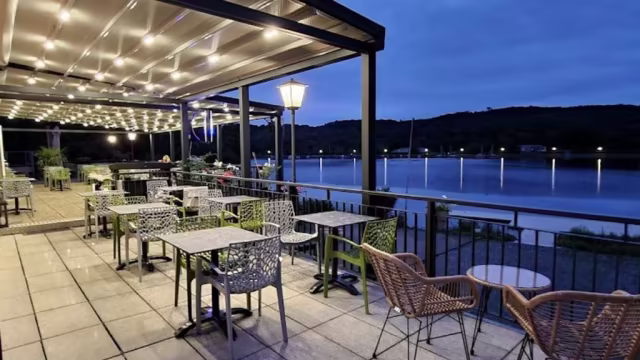 Außenbereich mit gemütlicher Beleuchtung, verschiedenen Sitzmöglichkeiten und einem ruhigen Wasserblick, ideal für einladende Mahlzeiten.