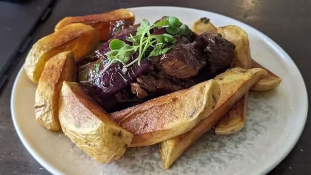 Carne estofada sobre una cama de gajos de papa dorados y crujientes, decorada con microgreens frescos.