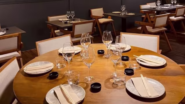 Interior de restaurante con mesa redonda de madera, decorada con platos elegantes y palillos, sugiriendo cocina asiática y una experiencia gastronómica de alta calidad.
