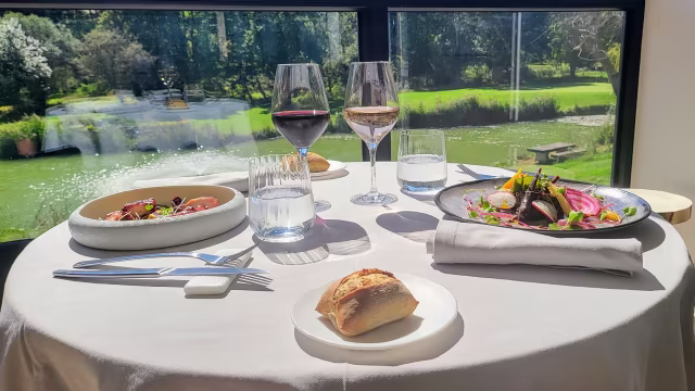 Deux plats principaux élégamment présentés : à gauche, des viandes séchées finement tranchées avec des jeunes pousses et des fleurs comestibles, accompagnées d'une épaisse sauce et acidulée ; à droite, une protéine grillée avec un mélange de légumes rôtis, garnie d'herbes et d'une tranche de citron.