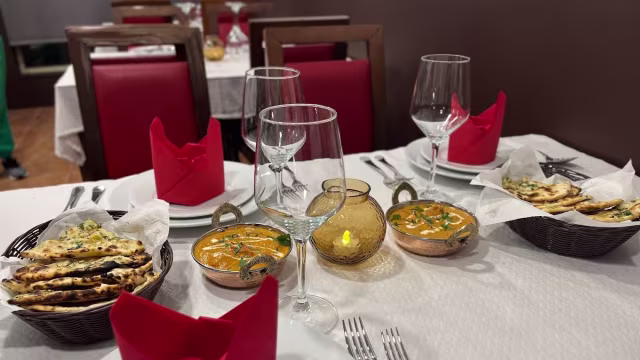 O cenário apresenta dois pratos de curry, possivelmente com um molho cremoso à base de tomate e pedaços de frango ou paneer, guarnecidos com coentros frescos, acompanhados de naan dourado e tostado.