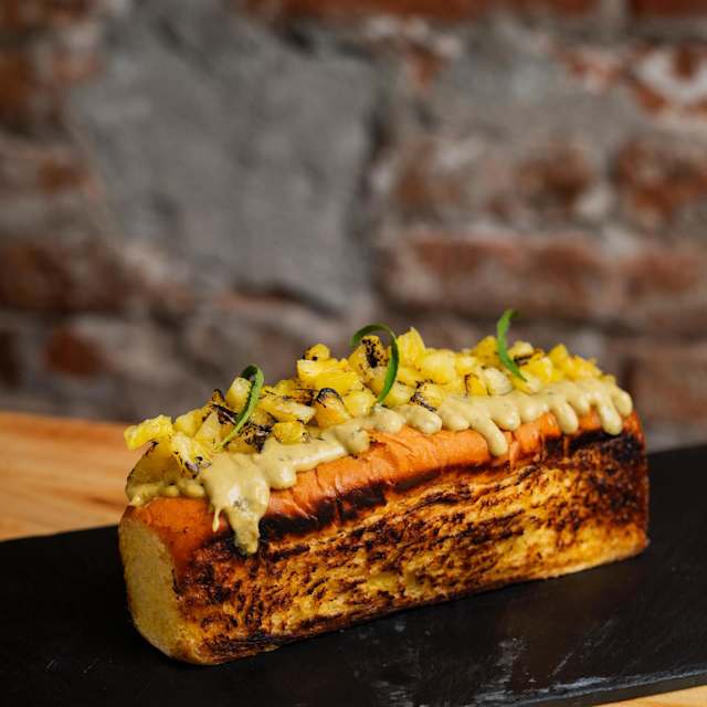 CRAB-ROLL Rico brioche tostado relleno de carne de centollo sazonado en mantequilla de ajo y jenjibre. Salsa Uchucuta peruana y piña marinada y flambeada con mezcal.