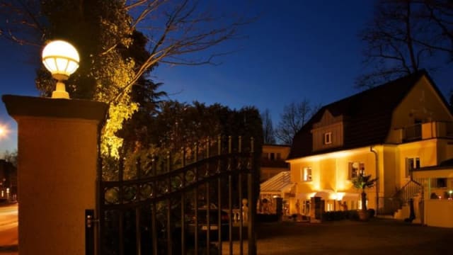 Charmante Restaurantfassade mit warmem gelben Anstrich, sanfter Beleuchtung und einem einladenden Ambiente, umgeben von Grün.