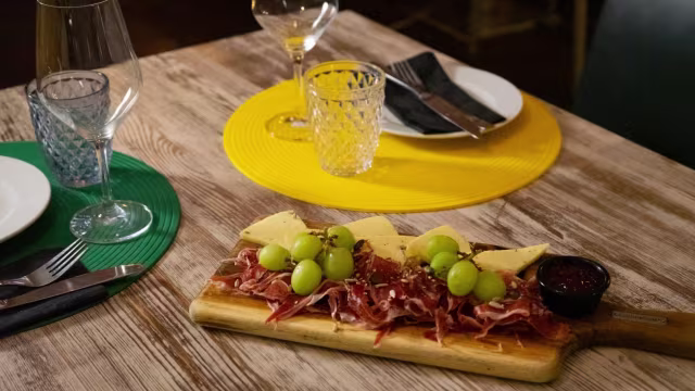 Tabla de charcutería con embutidos curados, uvas frescas, quesos cremosos y chutney dulce.