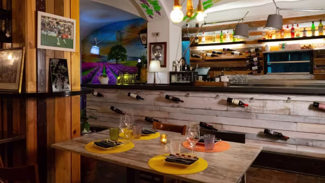 Interior de restaurante acogedor con encanto rústico, paredes de paneles de madera, mural paisajístico y barra con bebidas coloridas, creando un ambiente cálido y acogedor.