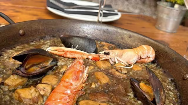 Paella de mariscos con arroz dorado al azafrán, camarones, mejillones y trozos de pollo, decorada con hierbas frescas.