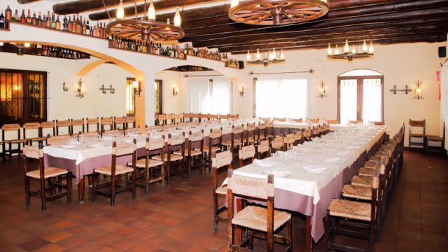 Interior de restaurante amplio y acogedor, con mesas elegantes, vigas de madera y candelabros rústicos, ideal para reuniones y celebraciones.