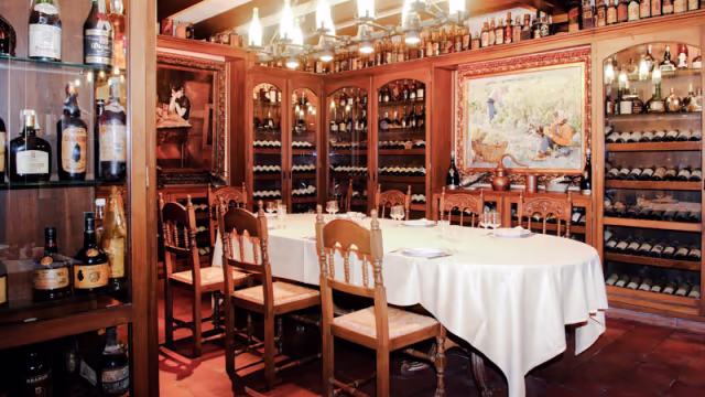 Interior acogedor de un restaurante con mesa de madera, sillas rústicas y ambiente cálido, ideal para compartir comidas.