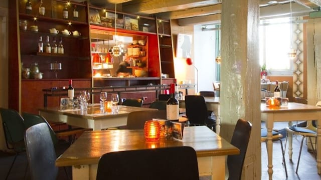 Gezellige restaurantinterieur met een warme ambiance, houten tafels en stoelen, een open keuken op de achtergrond en sfeervolle verlichting.