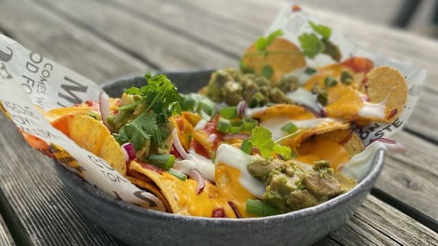 Rijke portie nacho's met gesmolten cheddar, guacamole, zure room, groene uien, rode uien en koriander, wat zorgt voor een bevredigende snack.
