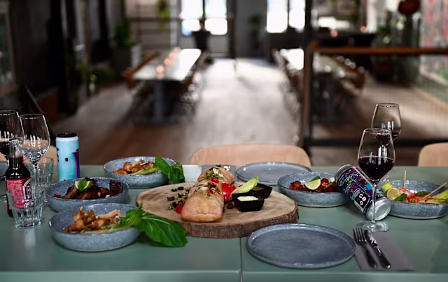 Mooi gepresenteerde tafel met een groot lichtgeroosterd zalmfilet, gegarneerd met verse kruiden en limoenpartjes, omringd door kleinere borden met een assortiment van hapjes, waaronder knapperige kippenvleugels en een kleurrijke salade met cherrytomaten en groenten.