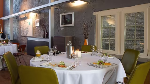 Moderne restaurantinterieur met een elegant gedekte ronde tafel, omringd door groene stoelen en sfeervolle verlichting.