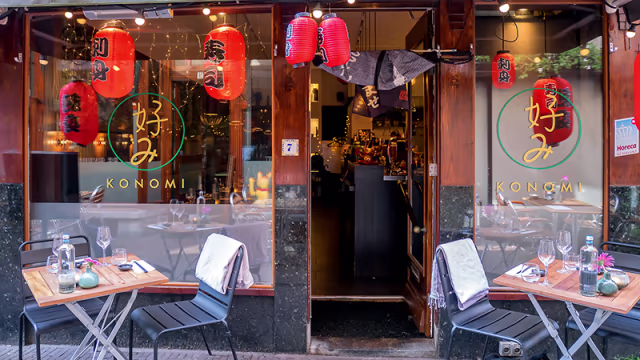 De buitenkant van het Japanse restaurant "Konomi" met grote glazen ramen, traditionele rode lantaarns en een combinatie van moderne en traditionele Japanse esthetiek.