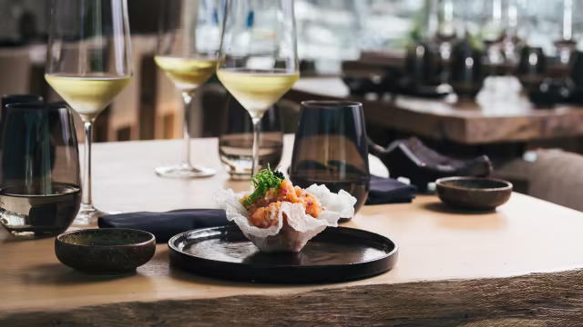 Uma crosta delicada e crocante recheada com uma mistura colorida de mariscos finamente picados, incluindo camarão e possivelmente abacate, guarnecida com ervas frescas e um toque de citrinos.