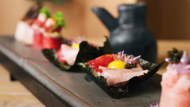 Sushi elegante com fatias delicadas de atum e salmão sobre folhas de nori, guarnecido com ovo de codorniz e caviar, acompanhado de rolos recheados com legumes e frutos do mar, decorados com ervas frescas e flores comestíveis.