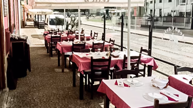 Área de refeições ao ar livre com mesas cobertas por toalhas de mesa xadrez vermelho e branco, rodeadas de vegetação e plantas em vasos, criando um ambiente acolhedor para refeições ao ar livre.