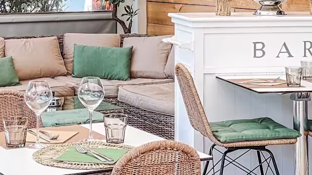Intérieur de restaurant chaleureux avec des coussins confortables, des chaises en osier et un bar au comptoir blanc, créant une ambiance accueillante pour des rencontres décontractées.