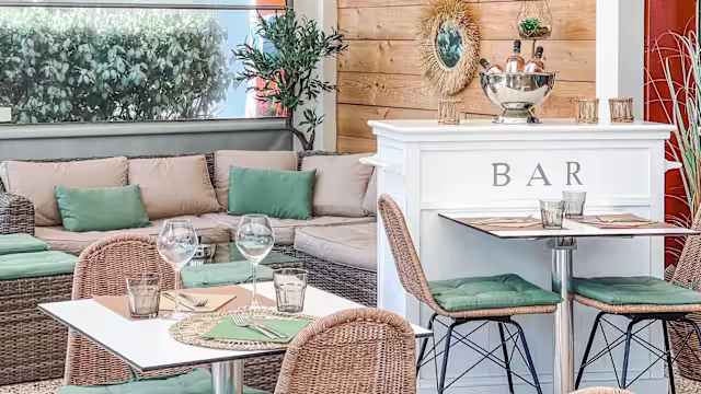 Intérieur de restaurant élégant et décontracté, avec des tables bien dressées, des chaises en osier, un coin salon confortable et un bar bien approvisionné, le tout dans une ambiance chaleureuse.